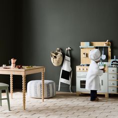 a small child in a white coat is playing with a toy kitchen set and table