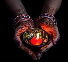 two hands holding a lit candle in the shape of a heart with hendi tattoos on it