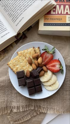 a white plate topped with fruit and crackers on top of a table next to an open book