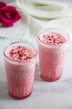 two glasses filled with pink liquid sitting on top of a white table next to a flower