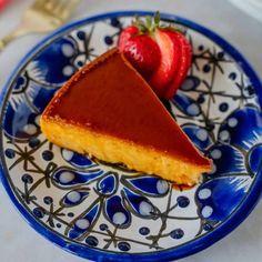 a slice of cheesecake on a blue and white plate with strawberries next to it