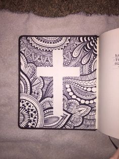 an open book with a cross drawn on the cover in black and white, sitting on a bed