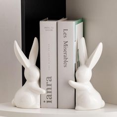 two white bunny figurines sitting next to each other on top of a shelf