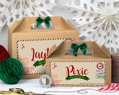 two boxes with green bows on them sitting next to christmas decorations and paper snowflakes