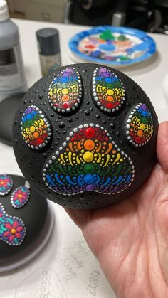 a hand holding a painted rock that looks like a dog's paw with colorful designs on it