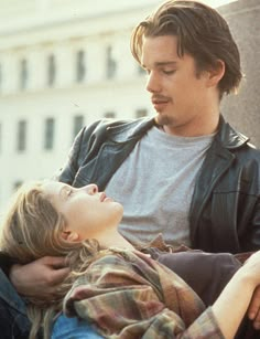 a man sitting next to a woman on top of a bench in front of a building