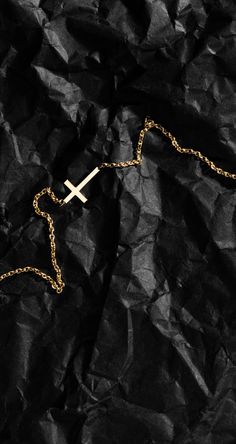 a cross on a chain laying on top of black crumpled paper with the word jesus written across it