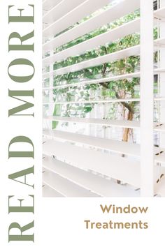 a window with white blinds in front of it and a green tree behind the blind