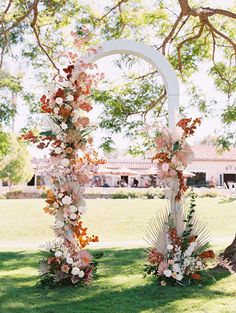 an arch decorated with flowers and greenery in front of a tree at a wedding