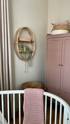 a baby's crib with a pink blanket on it and a wicker basket hanging from the wall