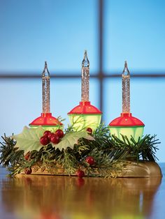 three christmas lights sitting on top of a wooden table next to holly and red berries