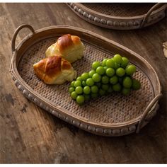 two trays with bread, grapes and croissants on them sitting on a wooden table