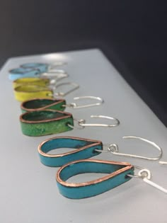 five pairs of earrings are lined up on a white surface, each with different colors