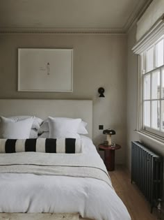 a white bed with black and white pillows in a bedroom next to a radiator