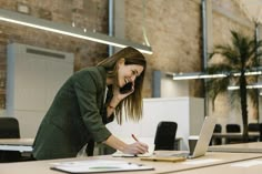 a woman talking on her cell phone while using a laptop computer in an office setting