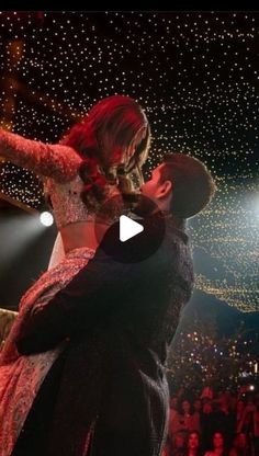 a man and woman kissing in front of an audience at a concert with lights on the ceiling