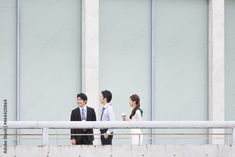 three people standing on a balcony talking to each other and one person holding a coffee cup