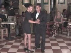 two people are dancing on a checkered floor in a room full of tables and chairs