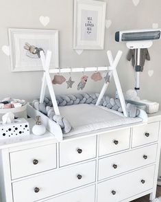 a baby crib in the corner of a room with white dressers and pictures on the wall