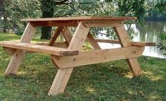 a wooden picnic table sitting on top of a lush green field next to a lake