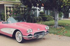 an old pink and white car parked in front of a house next to a tree