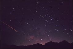 the night sky is filled with stars and there are mountains in the foreground, as well as an airplane flying overhead