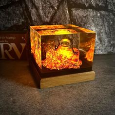 an illuminated cube with glasses on it sitting on top of a wooden stand next to a rock wall