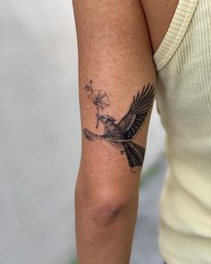 a woman's arm with a bird and flower tattoo on the left side of her arm