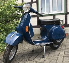 a blue scooter parked in front of a house on a brick sidewalk next to bushes