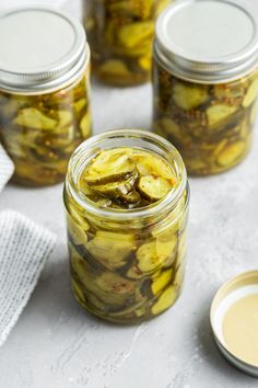 pickles in glass jars on a white surface next to a jar of mustard sauce