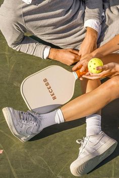 two people sitting next to each other holding tennis balls and racquets on a court