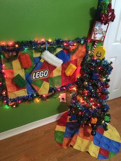 a christmas tree decorated with legos and lights next to a wall hanging on a green wall