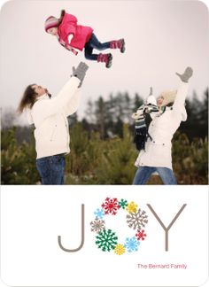 two people holding up a child in the air with joy written on it and snowflakes all around them