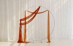 an orange drape draped in front of a white curtain and round object on the floor