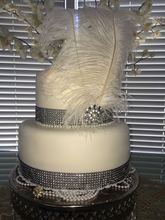 a three tiered wedding cake with white feathers and diaper bling on top