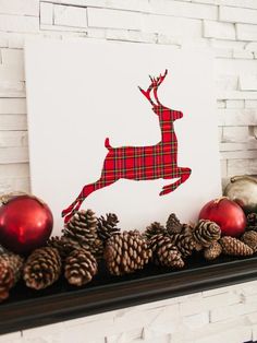 a fireplace mantel decorated with pine cones, ornaments and a paper cut out of a deer