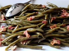 green beans with bacon on top and a spoon next to it, sitting on a white plate