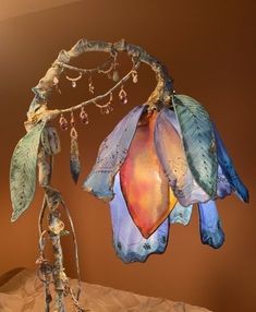 a glass flower hanging from a tree branch with beads and leaves on it's end