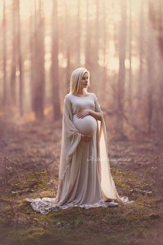 a pregnant woman in a long dress standing in the woods with her belly wrapped up