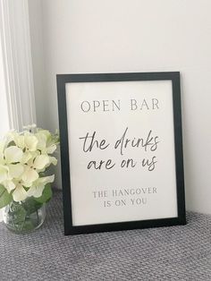 an open bar sign sitting on top of a table next to a vase with flowers