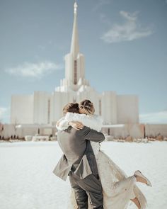 a bride and groom hug in front of the mormon temple