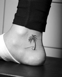 a small palm tree tattoo on the side of a woman's foot, which has a wave coming out of it