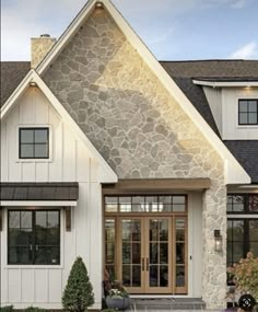 a white house with black shingles and stone on the front door is pictured in this image