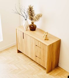 a wooden cabinet sitting on top of a hard wood floor next to a vase filled with flowers