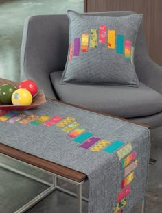 a gray chair with a colorful table runner next to it and a bowl of fruit