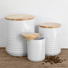 three white canisters with wooden lids are sitting on a wood floor in front of a white wall