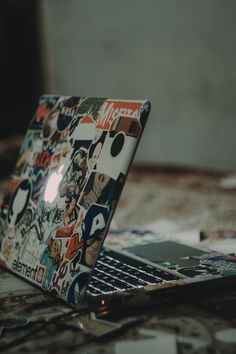 an open laptop computer sitting on top of a bed covered in sticker decals