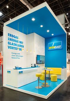 an exhibition stand with blue and white walls, yellow chairs and tables in front of it