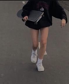 a woman walking down the street with a skateboard in her hand and wearing a black sweatshirt