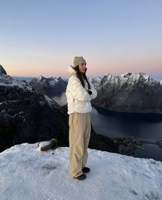 a woman standing on top of a snow covered mountain next to a body of water